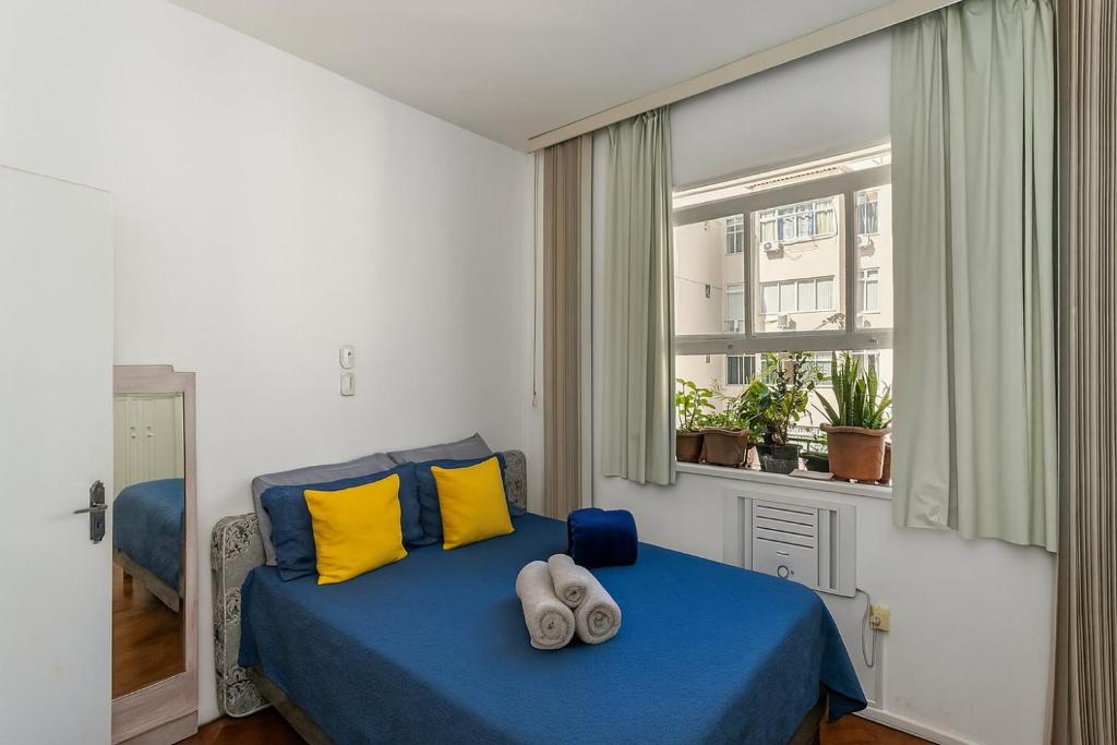 a bedroom with a blue bed with yellow pillows and a window at Copacabana Clássica! Praia e Conforto in Rio de Janeiro