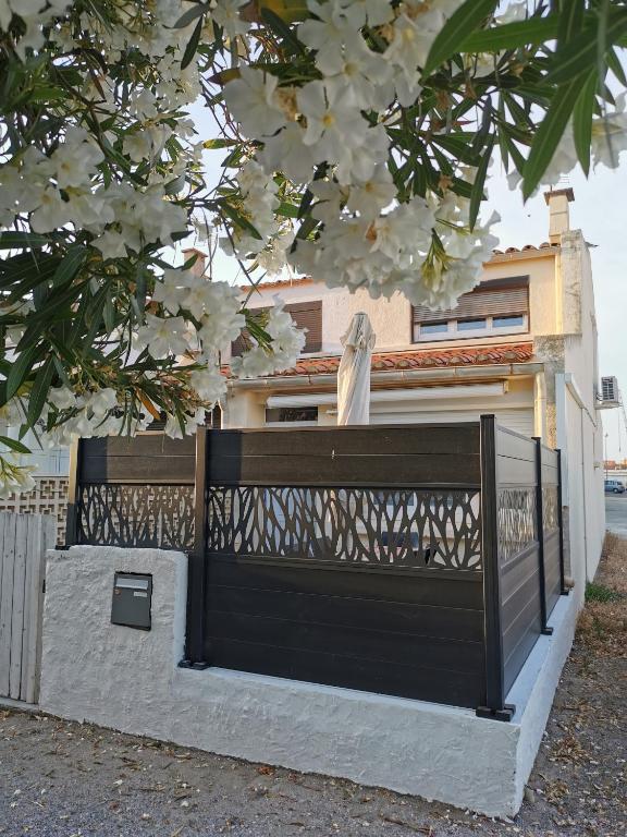 un portail noir devant une maison avec un arbre en fleurs dans l'établissement Pavillon T3 proche de la plage TERRASSE GARAGE PARKING, à Port-la-Nouvelle