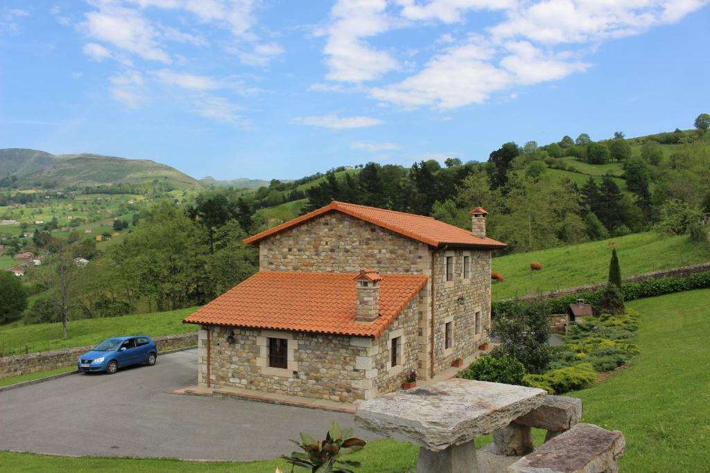 un pequeño edificio de piedra con un coche aparcado en un campo en La Cabaña del Abuelo de Selaya, en Selaya