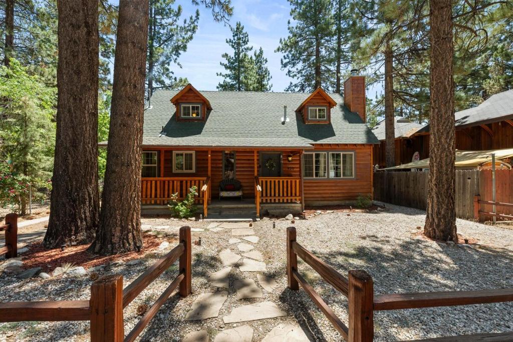 eine Blockhütte im Wald mit einem Zaun in der Unterkunft Bear Cub Cabin with Hot Tub, Outdoor Patio w BBQ! in Big Bear City Airport