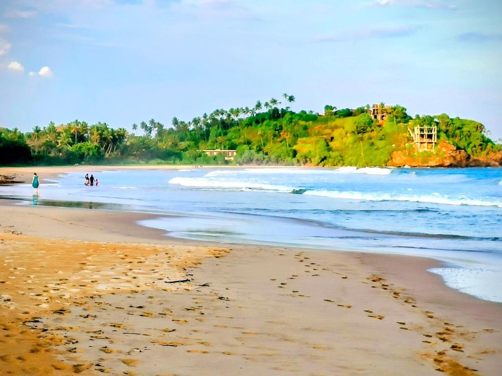 a beach with people walking on the sand and the ocean at Stargate Villa in Talalla