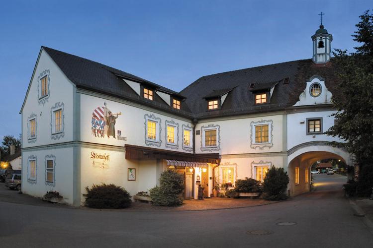 - un grand bâtiment blanc avec une arche en face dans l'établissement Hotel Restaurant Klosterhof, à Gutenzell-Hürbel