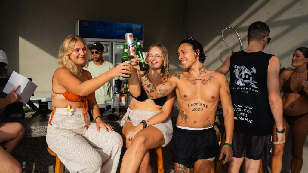 a group of women sitting around a man holding a beer at The Farm Nusa Party Hostel in Nusa Penida