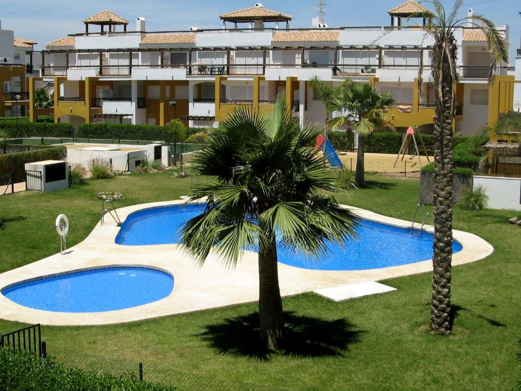 a swimming pool with a palm tree in front of a building at Apartamento VenAVera Playa Lomas del Mar I G1-1A Piscina Cubierta Pádel y WIFI in Vera
