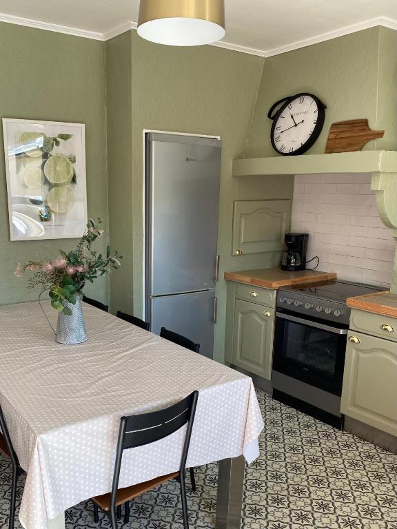 une cuisine avec une table et une horloge au mur dans l'établissement Aux Petits Bonheurs, à Grandcamp-Maisy