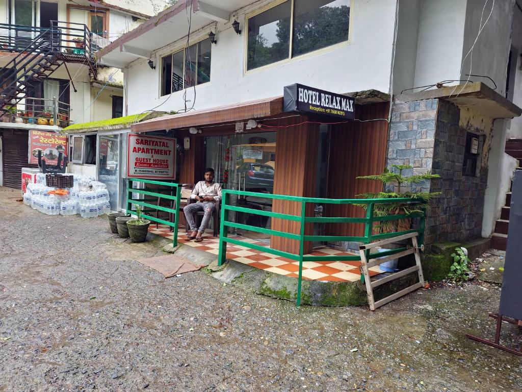un hombre sentado en un banco fuera de un edificio en Hotel Relax Max Sariyatal Nainital, en Nainital