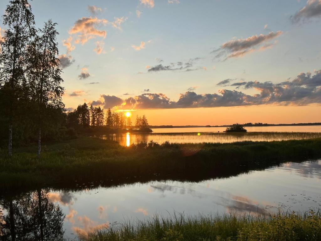 a sunset over a body of water with trees at Cozy cottage on lake in Iokela