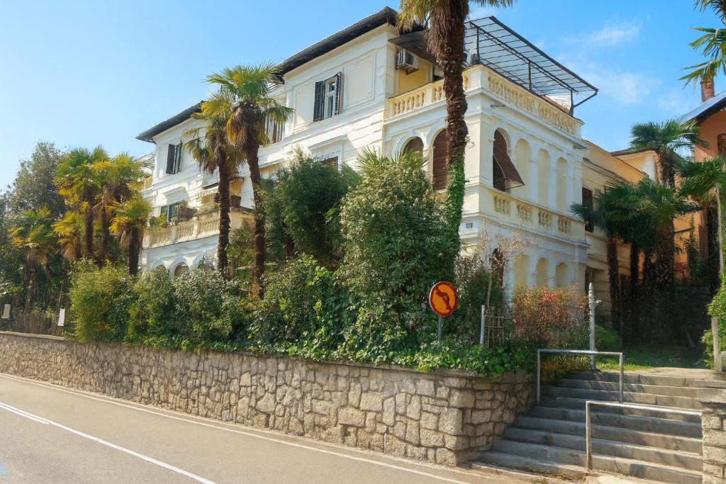 een wit gebouw met palmbomen voor een straat bij Apartment Opatija 365, steps from the sea & city center, free street parking in Opatija