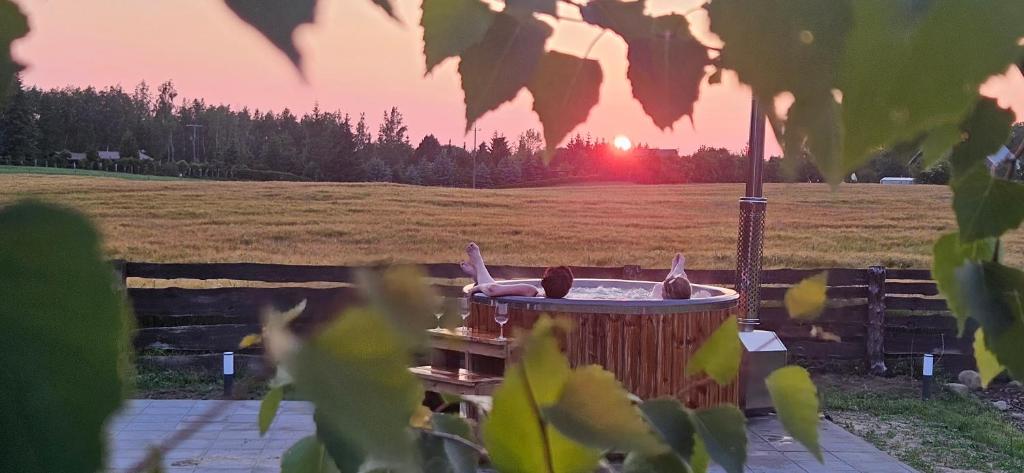 a person laying in a hot tub with the sunset in the background at Mazurkowo domek Gaj-Grzmięca in Zbiczno