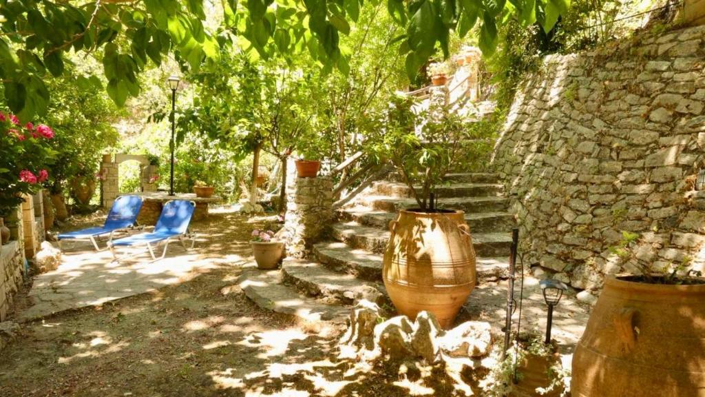 ein Garten mit zwei blauen Stühlen und einer Steinmauer in der Unterkunft Angela's River Paradise Cottages in Mixórrouma