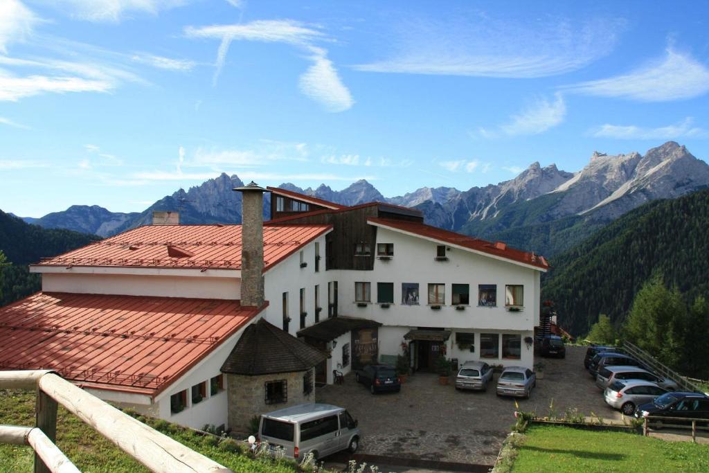 a building with cars parked in a parking lot with mountains at HG Hotel La Caminatha in Val di Zoldo