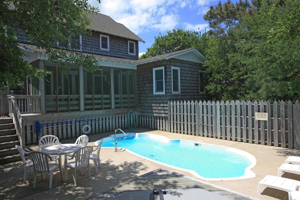 a swimming pool with chairs and a table and a house at Reminiscent in Nags Head