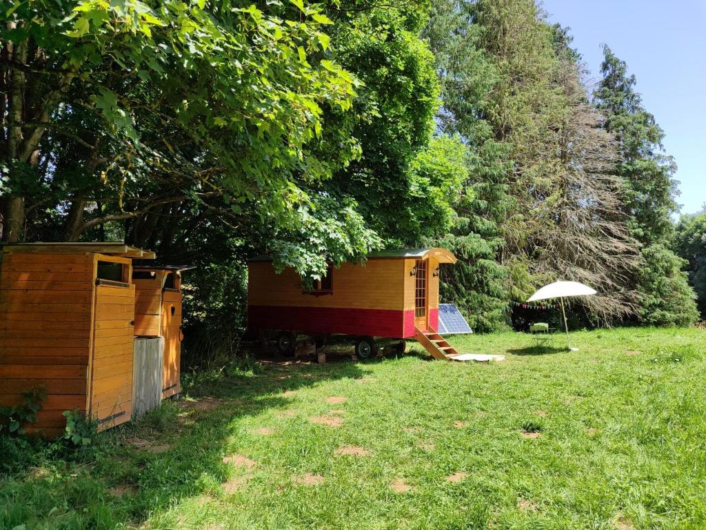 a small house and an umbrella in a yard at Roulotte au pied des volcans, cuisine et sdb de plein air in Orcines