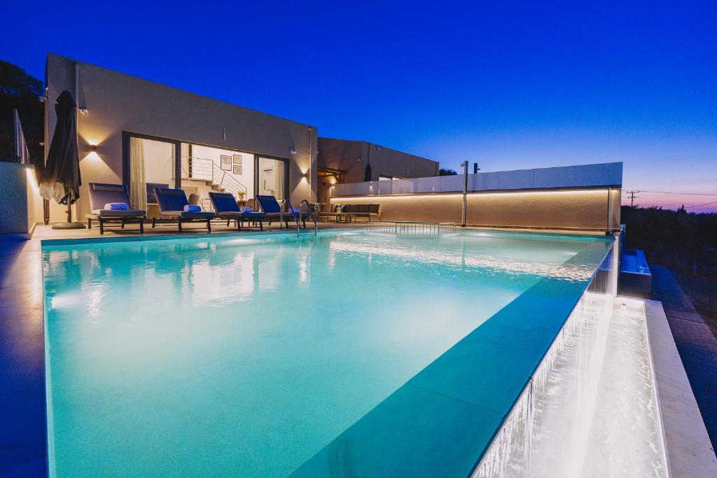 a swimming pool with blue chairs and a building at Pasiphae Luxury villa in Agia Pelagia