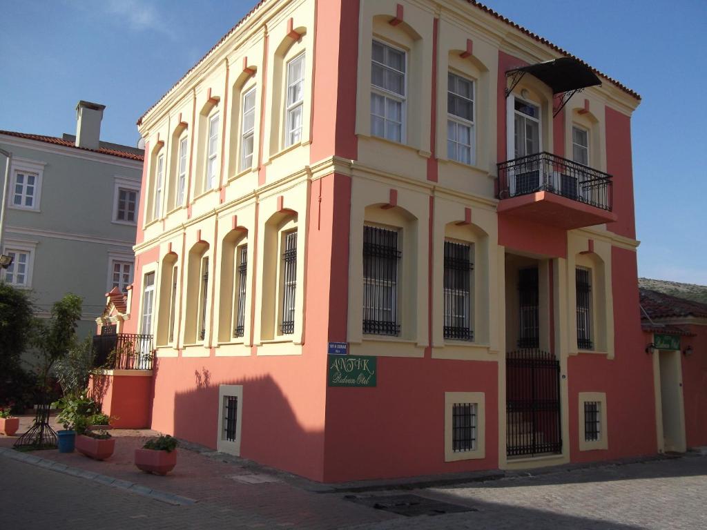 a red and yellow building with a woman on a balcony at Antik Ridvan Hotel in Çeşme