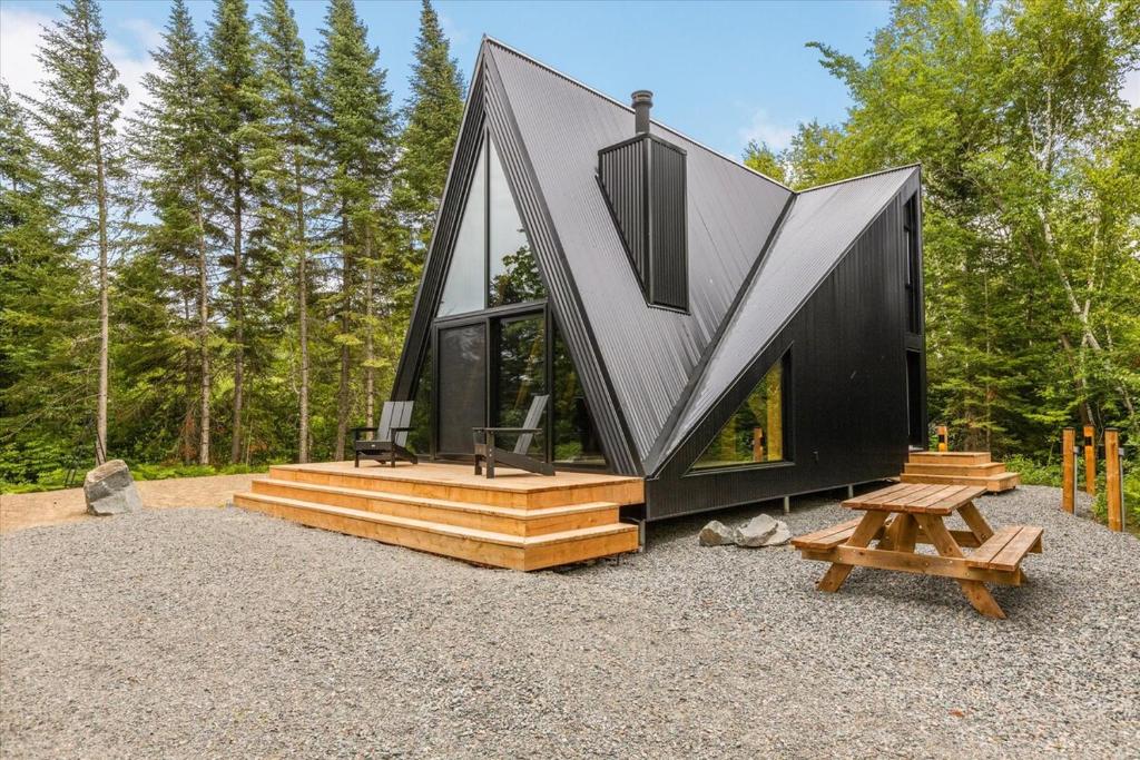 Una pequeña casa con techo negro y escalones de madera. en La Cabine Hygge, en Saint Roch de Mekinac