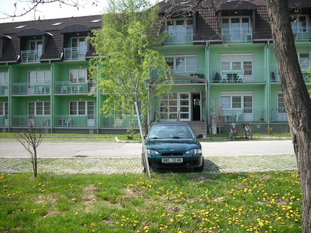 un coche aparcado frente a un edificio verde en Aba és Andrea Apartmanok, en Sárvár