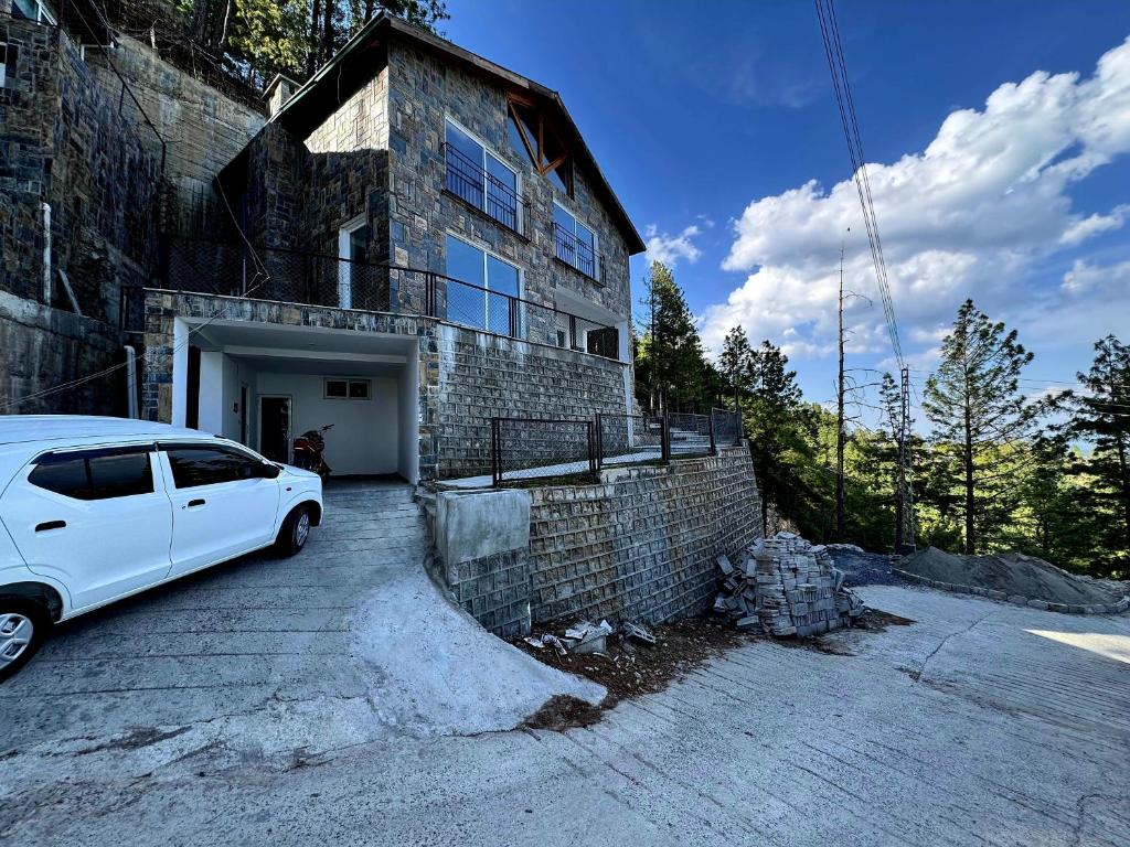 Haven Lodge Khaira Gali - Pine Ridge Residences #4 في Khaira Gali: سيارة بيضاء متوقفة أمام مبنى من الطوب