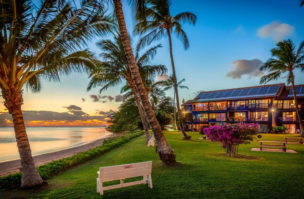 a building on the beach with palm trees and a bench at Castle at Moloka'i Shores in Kaunakakai