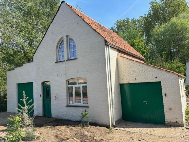 ein kleines weißes Haus mit grünen Garagentüren in der Unterkunft Duinenhuis Edgard in Koksijde