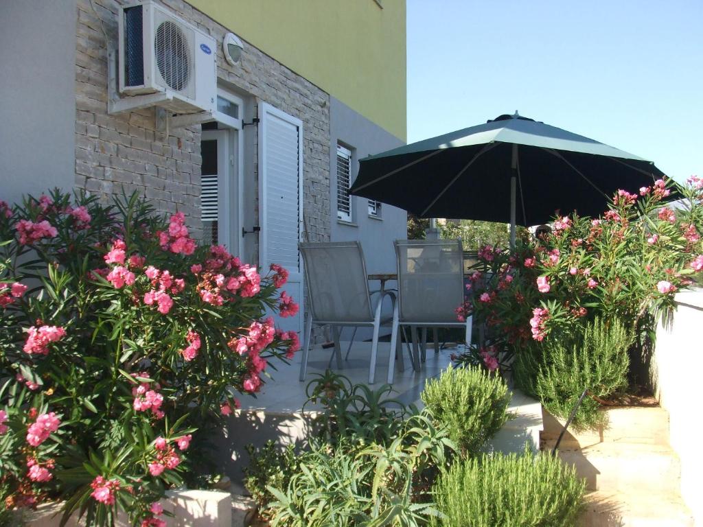 un patio con mesa, sombrilla y flores en Apartments Diva, en Novalja