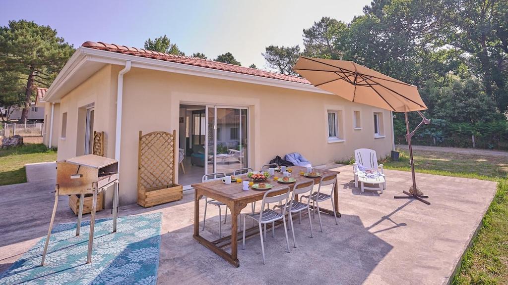 einen Tisch mit Stühlen und einen Regenschirm vor einem Haus in der Unterkunft Villa Jardin et forêt océan au Verdon in Le Verdon-sur-Mer