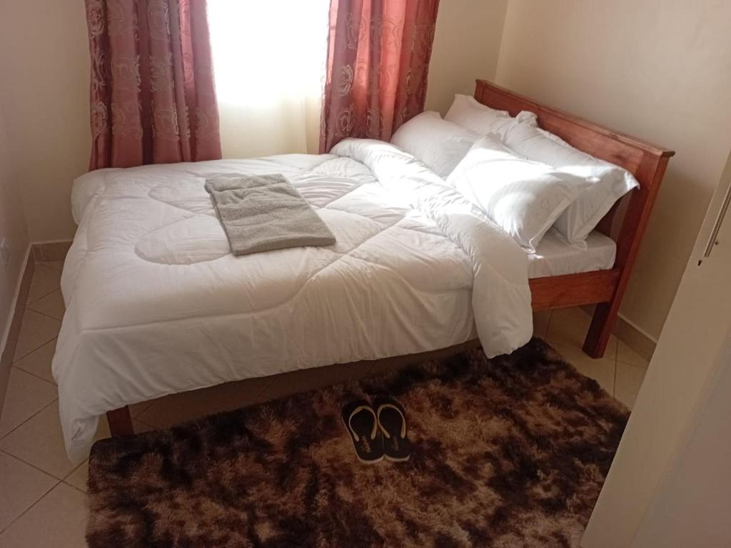 a bed with white sheets and a pair of shoes on it at Nyayo Embakasi Maisonette ZIPPYS Place in Nairobi