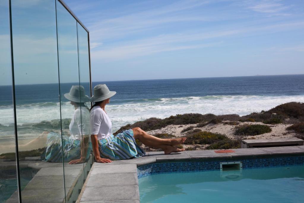 Dos personas sentadas junto a una piscina mirando el océano. en Seehuis, en Yzerfontein