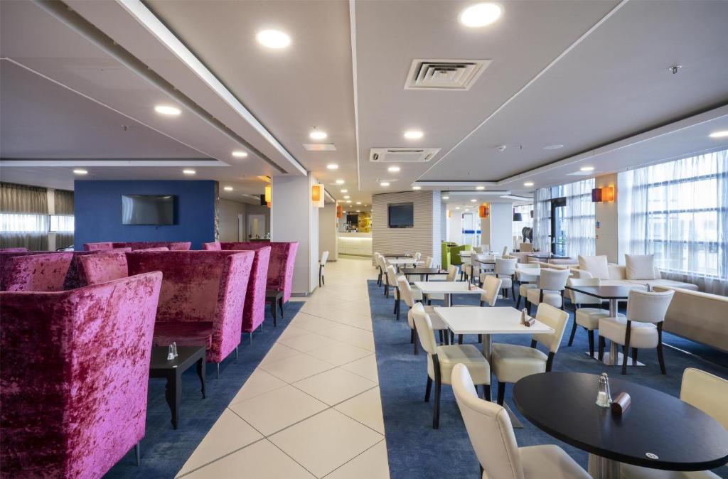 a restaurant with tables and chairs and purple booths at Hampton by Hilton Liverpool John Lennon Airport in Speke