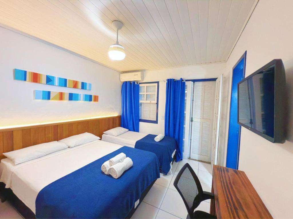 two beds in a room with blue curtains and a tv at Brothers Suites Centro Búzios in Búzios