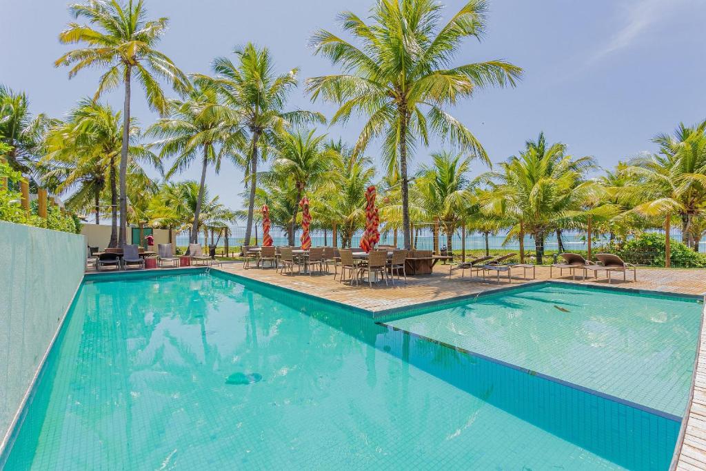 a swimming pool with palm trees and a beach at IT107 Apto Pé na Areia com com 3/4 - Itacimirim in Itacimirim