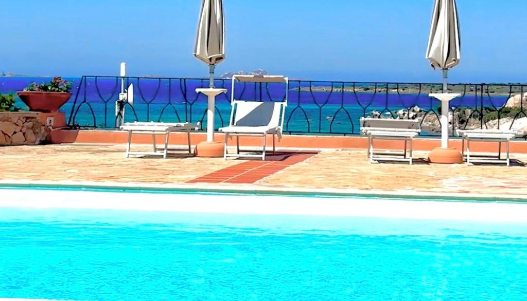 a swimming pool with chairs and umbrellas and the ocean at Studio In The Gulf of Marinella in Marinella
