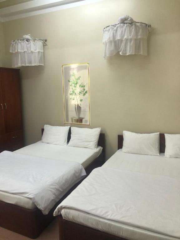 Dos camas en una habitación con sábanas y almohadas blancas. en Bảo Thịnh, en Da Lat