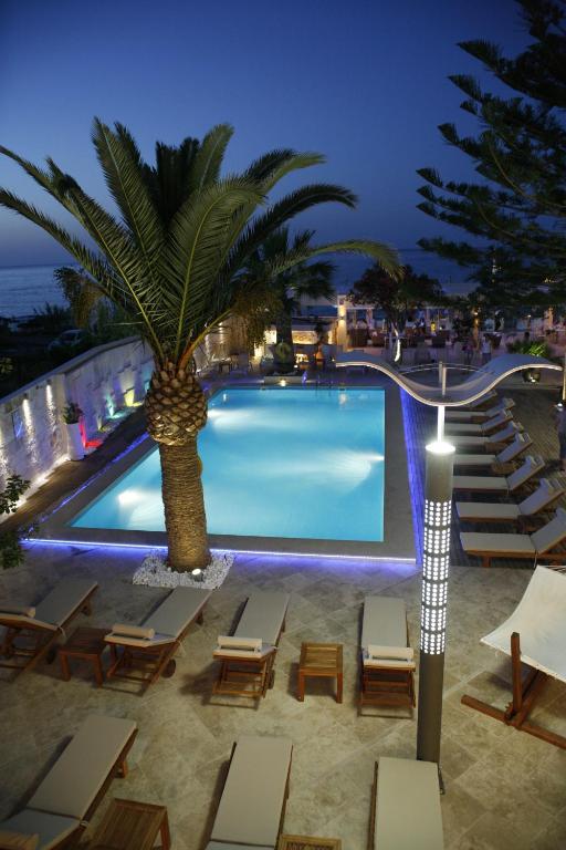 a swimming pool with chairs and a palm tree at Glaros Beach Hotel in Hersonissos