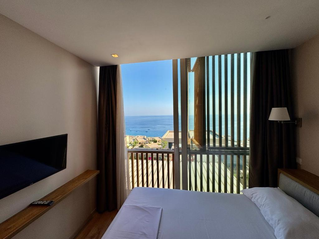 a bedroom with a large window with a view of the ocean at Green Condo Hotel Palase in Palasë