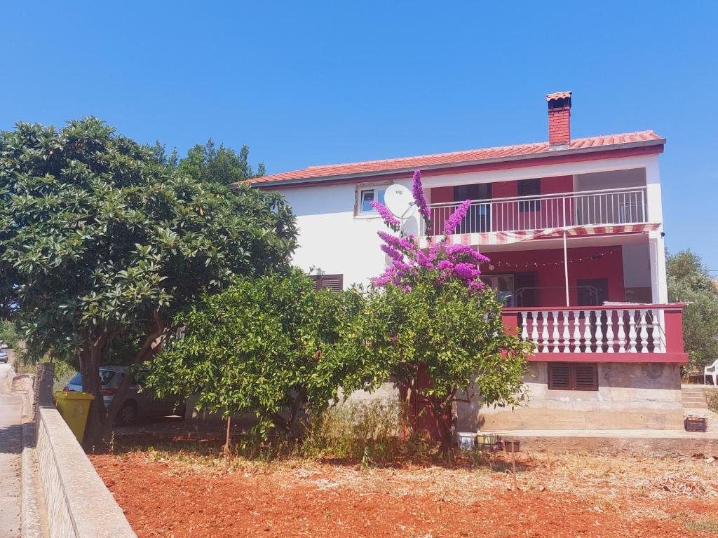 a white house with a balcony and purple flowers at Apartment Lordanic Zaglav, Dugi otok in Zaglav