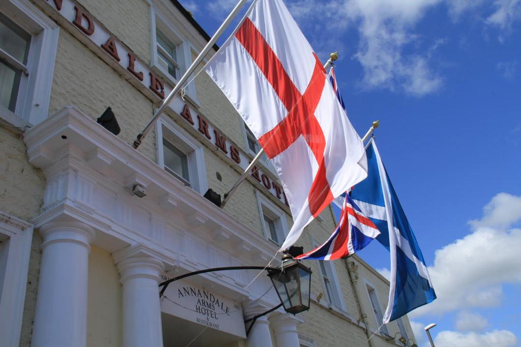 Zwei Flaggen fliegen vor einem Gebäude in der Unterkunft Annandale Arms Hotel in Moffat