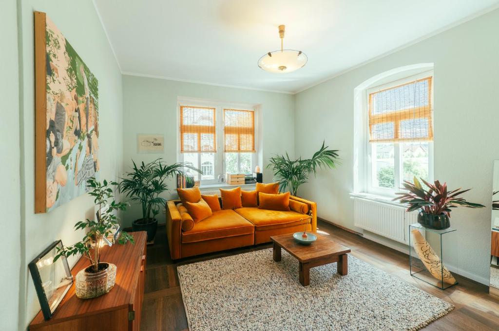 ein orangefarbenes Sofa in einem Wohnzimmer mit Pflanzen in der Unterkunft Ferienwohnung Feel Good Apartment - zentrale 65qm Design Fewo im Zittauer Gebirge - bahnhofsnah in ruhiger Lage in Zittau