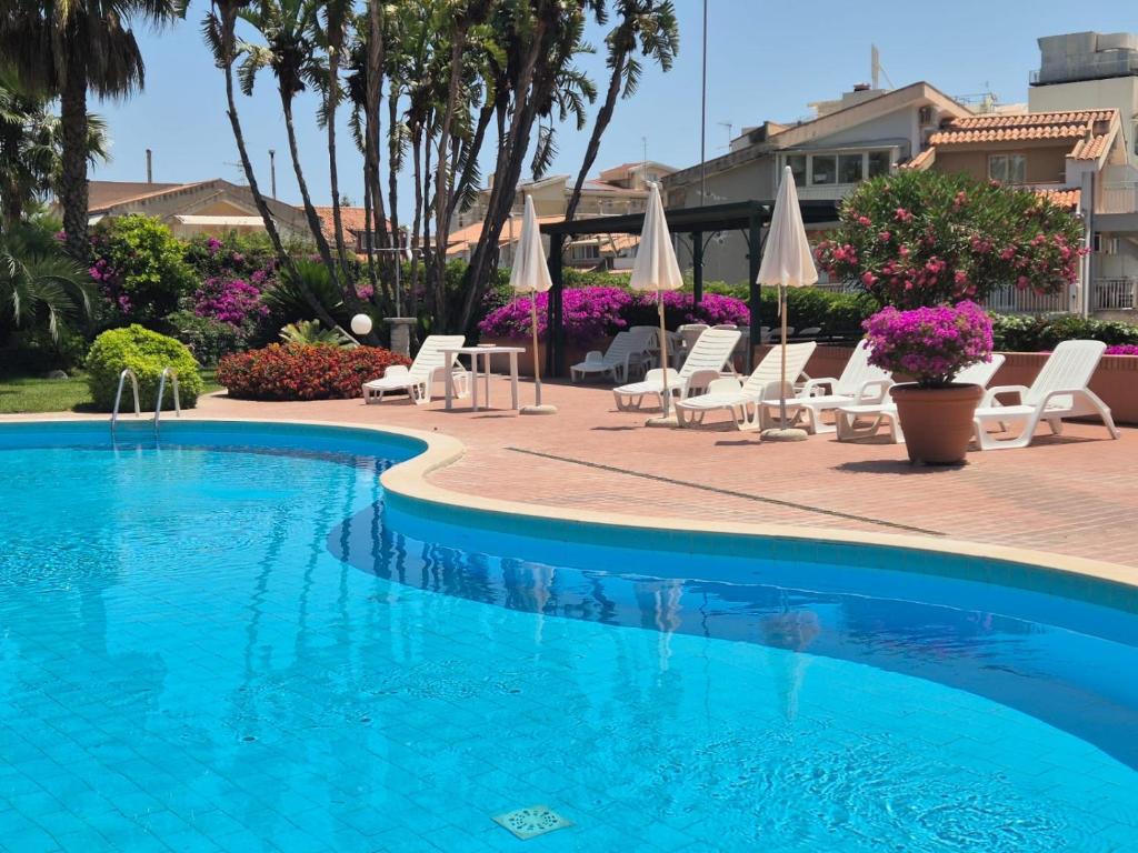 a swimming pool with white chairs and umbrellas at Orchidea Bianca in Giardini Naxos