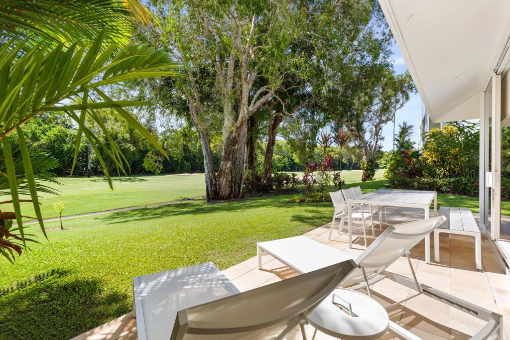 Un patio con sillas y mesas blancas y un jardín. en Mirage Resort Villa 128 with access to Sheraton Facilities, en Port Douglas