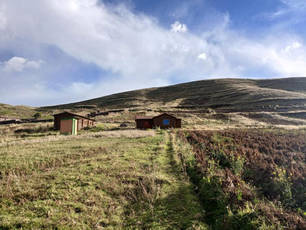 a field with two small buildings on a hill at Casa Serena in Yanaoca