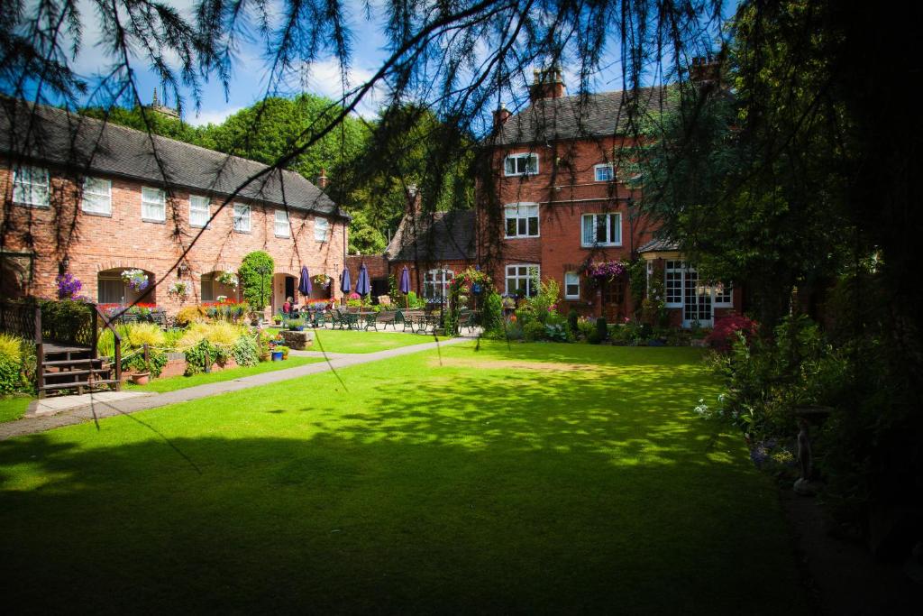 zielony dziedziniec z dwoma dużymi ceglanymi budynkami w obiekcie The Manor Guest House w mieście Cheadle