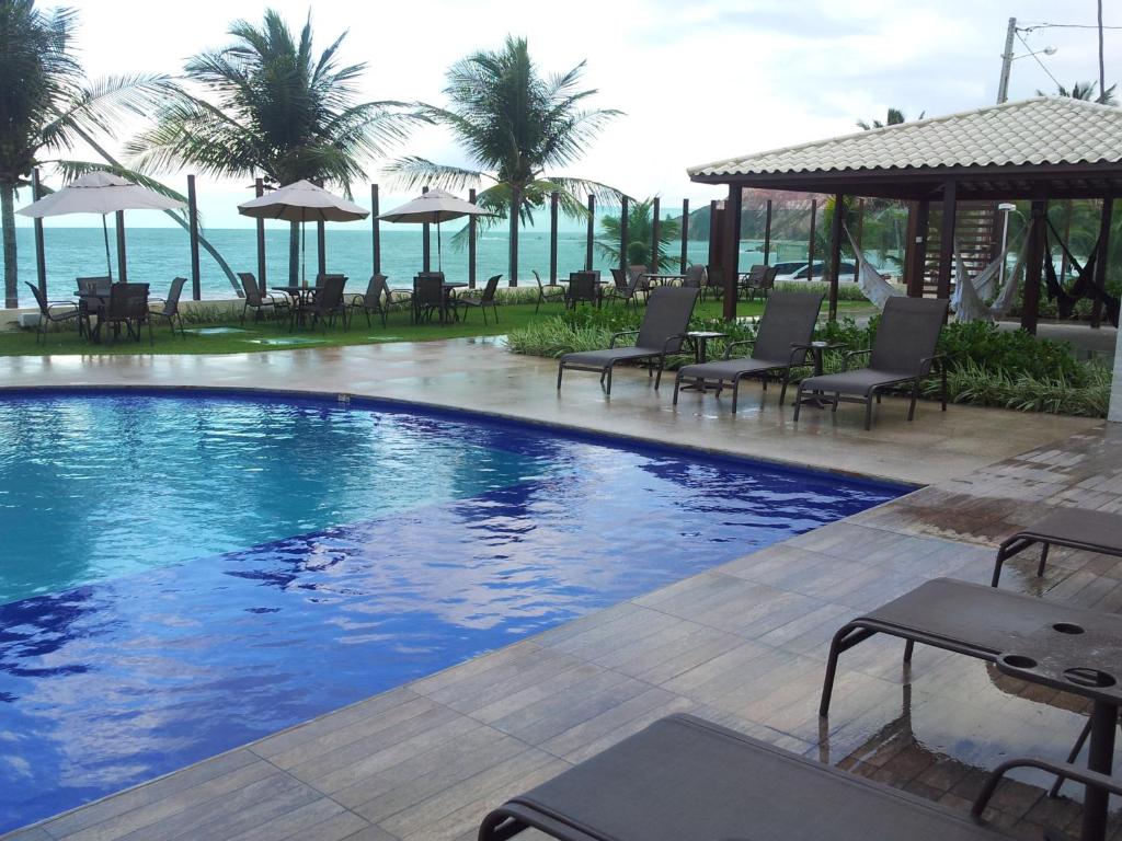 einen Pool mit Stühlen und das Meer im Hintergrund in der Unterkunft Praia Tabatinga AP Beira Mar com vista deslumbrante da praia in Jacumã