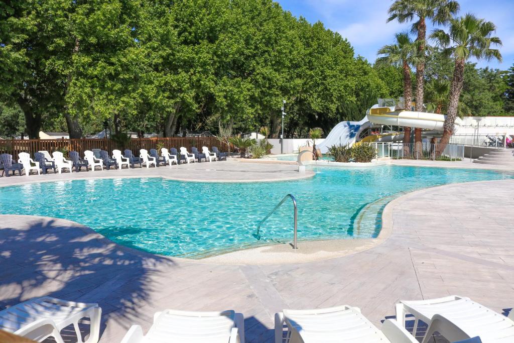 une piscine avec des chaises blanches et un toboggan dans l'établissement Talypso, à Agde