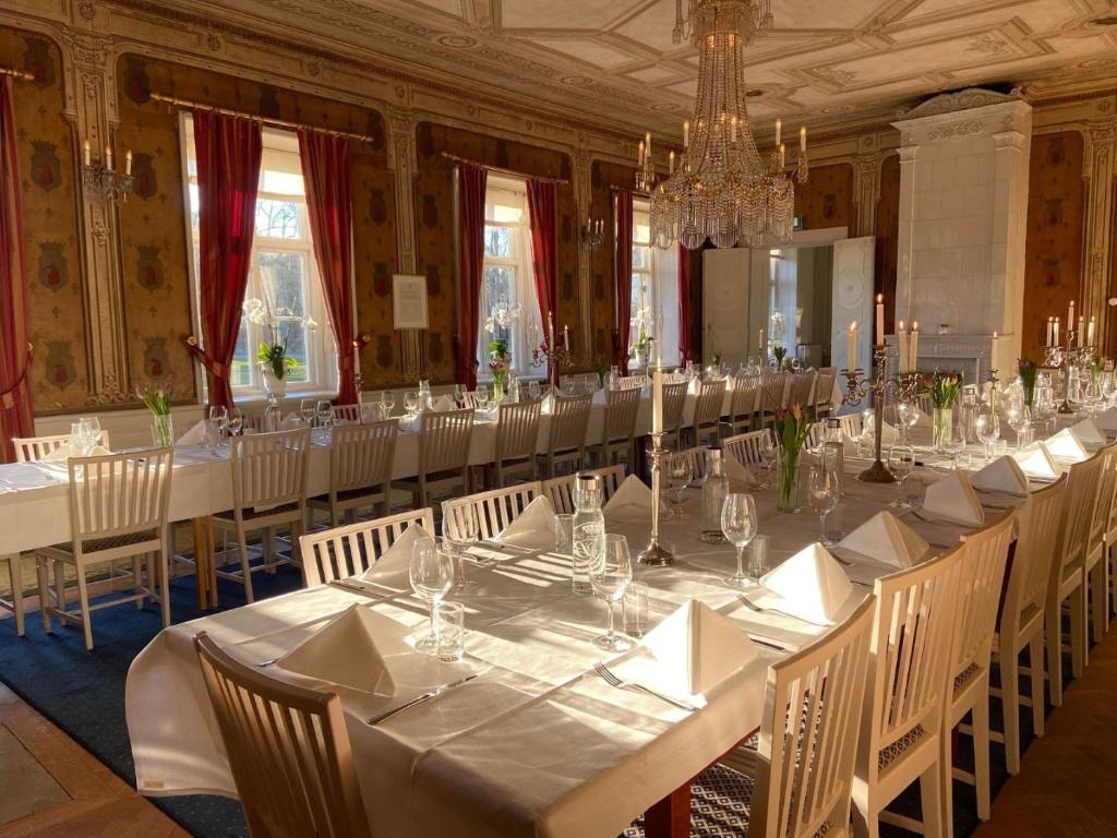 una lunga sala da pranzo con tavoli e sedie bianchi di Bäckaskog Slott a Fjälkinge