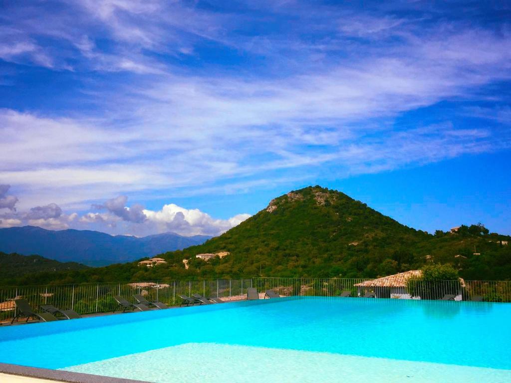 a blue swimming pool with a mountain in the background at Résidence Santa Giulia Park in Porto-Vecchio