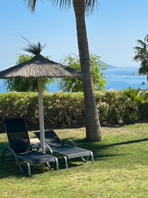 Dos sillas bajo una sombrilla y una palmera. en Chulera Beach townhouse sea views, en Manilva