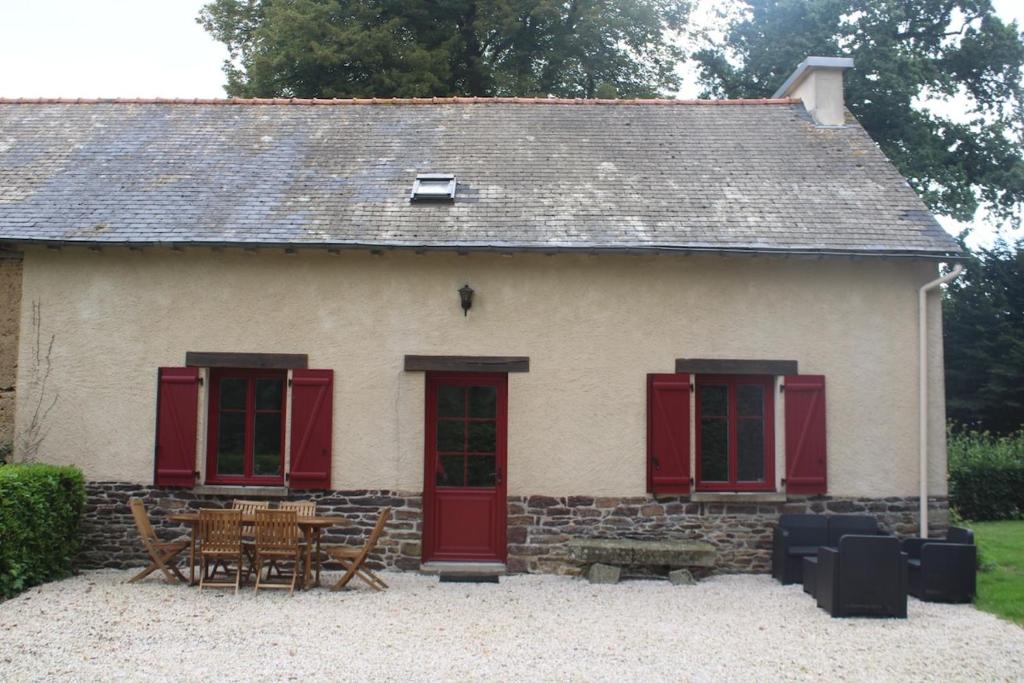 a house with red doors and a table and chairs at Gîte de vacances Brocéliande in Saint-Onen-la-Chapelle
