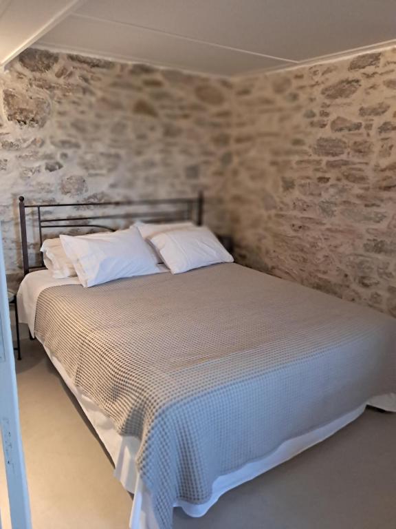 a bed with white pillows in a room with stone walls at Akros-cottage on mountain- ground floor in Stavrinídes