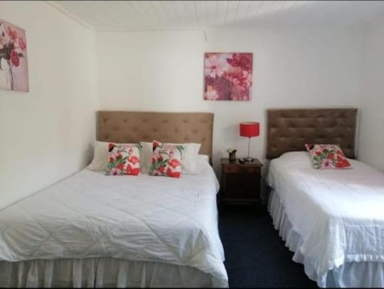 a bedroom with two beds with white sheets and red pillows at Hostal Nomade Renovado 2025 in Rancagua